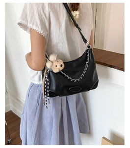 Detail of black faux leather tote with decorative chain and khaki plush bear charm
