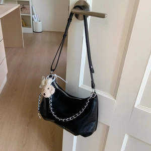 Detail of black leather half-moon bag with adjustable strap and cute bear charm