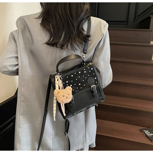 Detail of black retro PU leather shoulder bag with white rivets and teddy bear charm