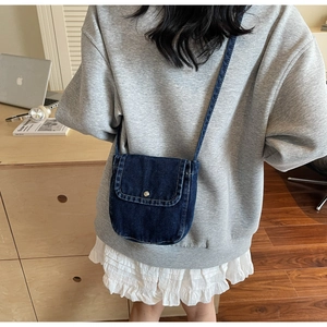 Detail shot of a dark blue denim crossbody mini square bag worn over a grey sweatshirt