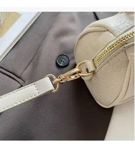 Detail of elegant cream cylinder bag featuring crocodile texture and golden hardware accents