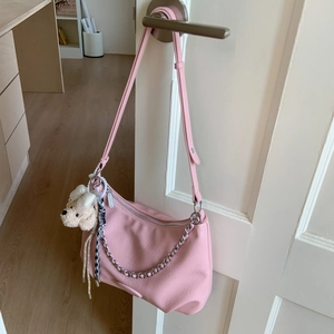 Pink crescent shoulder bag with silver chain detail and plush puppy charm on a door