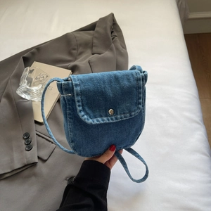 Detail of a mini washed denim crossbody bag with silver button snap closure and textured fabric