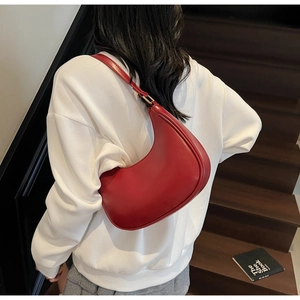 Close-up of a stylish red leather crescent underarm bag worn by a model in a casual setting