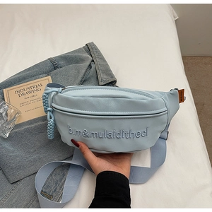 Détail d'un sac banane en similicuir bleu clair avec broderie sur fond en denim