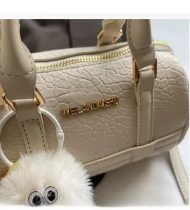 Detail of cream pillow bag with crocodile texture and gold logo with plush charm