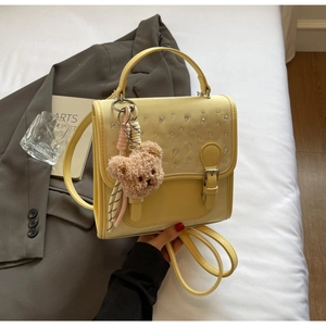 Detail of light yellow PU leather handbag with sparkling studs and brown bear charm