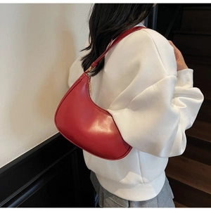 Close-up of a red leather hobo bag with gold zipper detail worn by a model in casual style