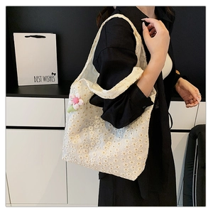 Close-up of white lace tote bag featuring daisy patterns and a pink floral charm detail