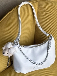 Minimalist white hobo bag with adjustable strap and silver chain on yellow sofa