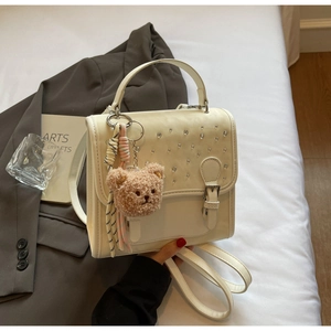 Detail of cream white PU leather backpack featuring rhinestones and a plush bear charm