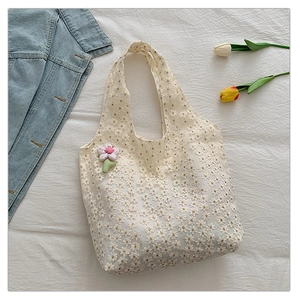 Detail of floral lace embroidery on cream canvas tote with a pink plush flower charm