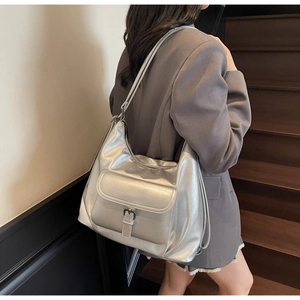 Detail of silver metallic tote bag showing buckle pocket and adjustable strap texture
