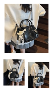 Detail of glossy black pleated handbag featuring pearl lace bow and slim shoulder strap