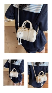 Detail view of cream Boston bag with embossed texture, gold logo and plush charm