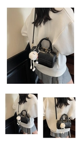 Close-up of black crocodile pattern Boston bag with gold zipper and plush ball charm