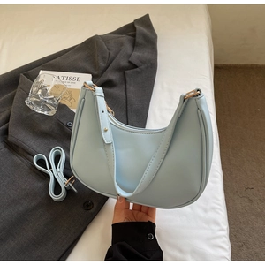 Detail of light blue hobo bag with gold hardware and adjustable strap on neutral background