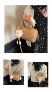 Detail of khaki boston bag with litchi texture, metal logo and white plush toy charm