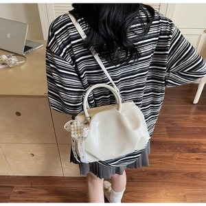Detailed shot of an off-white pleated handbag featuring elegant pearl and lace charms