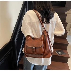 Detail of vintage brown leather hobo bag with a flap buckle pocket on a white shirt model