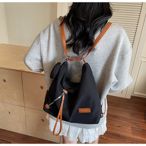 Detail of black nylon tote backpack with brown leather straps shown on a model