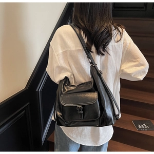 Close-up of black glossy leather tote bag with functional belt buckle pocket and strap detail