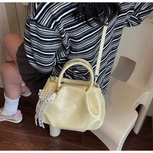 Model wearing a light yellow pleated cloud bag with a pearl bow charm in a home setting