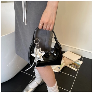 Close-up of black patent leather crescent bag with silver star charm in a lifestyle setting