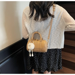 Close-up of khaki Boston bag with plush pendant on model over a wooden staircase