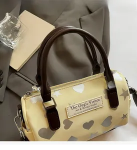 Dettaglio della borsa Boston con manici in pelle marrone e motivi a cuore su crema