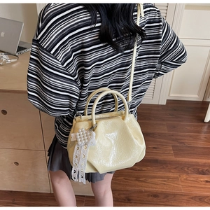 Detail of cream pleated crossbody bag with lace pearl pendant shown on shoulder
