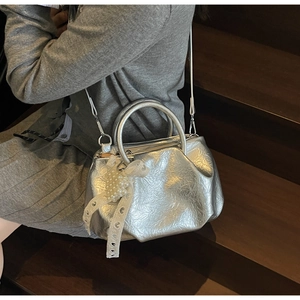 Detail of silver pleated handbag with pearl heart charm on model's lap in lifestyle setting