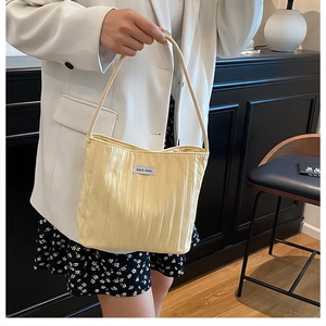 Close-up of light yellow pleated tote bag with woven label and long handles