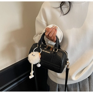 Close-up of black crocodile pattern boston bag with gold logo and plush monster charm