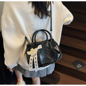 Close-up of black patent leather bag with pearl bow and white lace detail on a shoulder strap