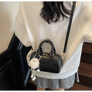 Detailed view of black pebbled leather pillow bag with cute plush doll charm accessory