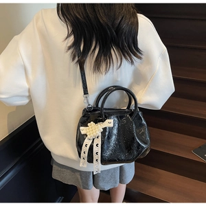 Detail of black glossy leather handbag with lace bow and pearl cluster on model back