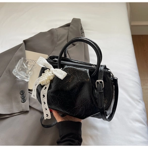 Close-up of black glossy pleated handbag featuring a white lace bow and pearl pendant