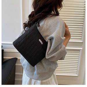 Detail of black pleated tote bag with square white woven label on the quilted surface