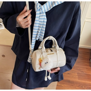 Close-up of elegant off-white crocodile embossed Boston bag with plush eye charm