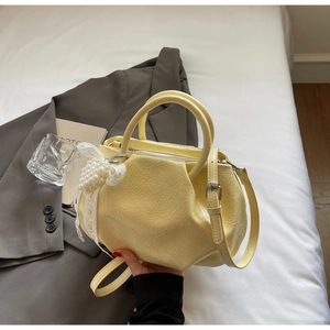 Detailed shot of yellow ruched handbag with lace bow and pearl charm on a grey suit