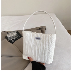 Detailed view of white pleated canvas tote bag with Ann's then brand label on a bed