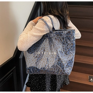 Détail d'un sac cabas bleu à motif léopard porté à l'épaule dans un escalier