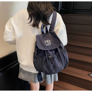 Detail of navy nylon backpack showing drawstring closure and MUT ING white embroidery