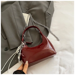 Detail of burgundy patent leather half-moon bag with silver metal chain and glossy finish