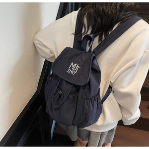Macro detail of navy nylon backpack featuring white MUTING embroidery and drawstring closure