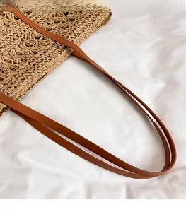 Detailed view of brown leather straps and woven straw texture on vacation tote bag