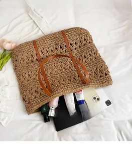Detailed view of woven straw tote bag with brown leather handles on white fabric
