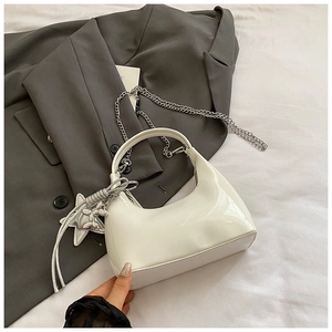 Detail of white glossy underarm bag with silver star and balloon dog charm over gray suit