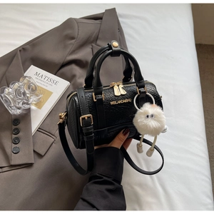 Close-up of black textured leather handbag with gold logo and plush charm detail